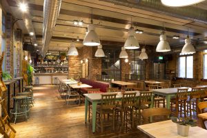 Interior of a traditional British food and drinks establishment with a modern twist. No people. Table, chairs, stools and bar counter seen with overhead lighting.