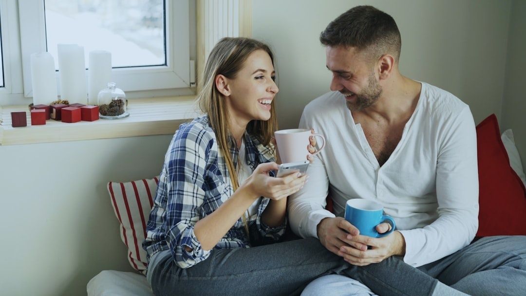 Par sitter tett sammen med kaffe og mobil i en hyggelig stue